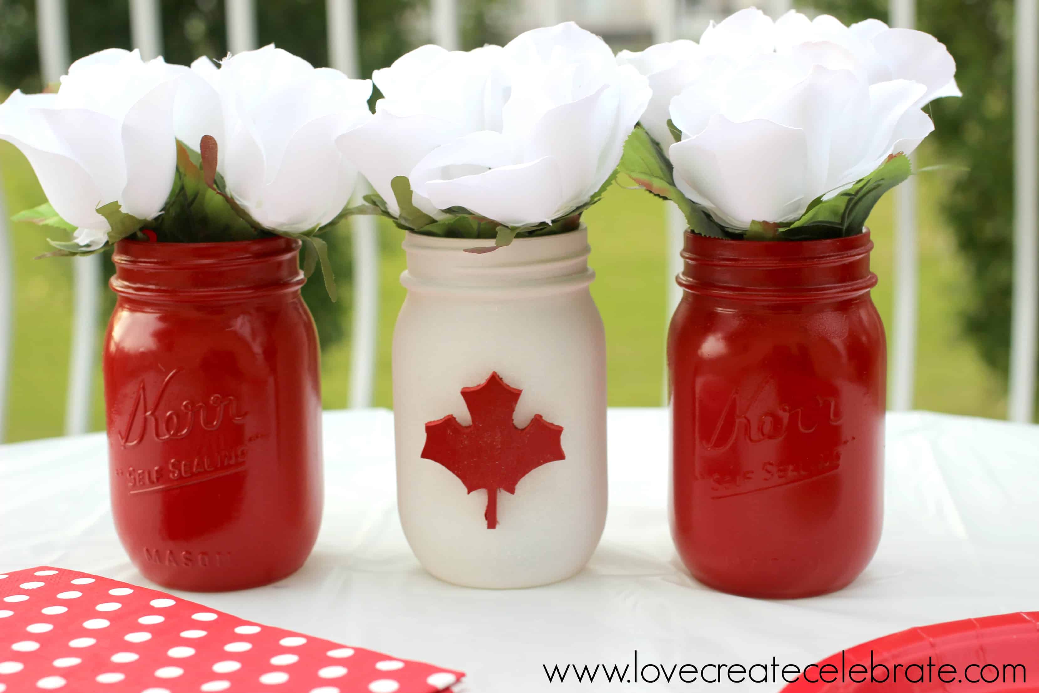 Mason jars painted red, white and red with a red maple leaf on the white painted jar 