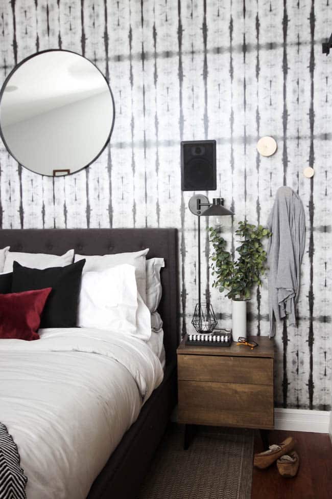 A beautiful Modern Master Bedroom Renovation Reveal! Gorgeous bold wallpaper, black, white and grey tones alongside wooden accent furniture. Ikea cabinets with a sliding barn door. And a white brick fireplace with a dark wooden mantel. Touches of blue and deep red finish the space perfectly. Beautiful transformation! 