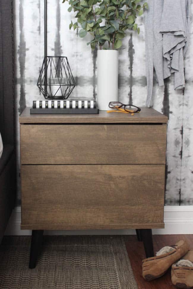 A beautiful Modern Master Bedroom Renovation Reveal! Gorgeous bold wallpaper, black, white and grey tones alongside wooden accent furniture. Ikea cabinets with a sliding barn door. And a white brick fireplace with a dark wooden mantel. Touches of blue and deep red finish the space perfectly. Beautiful transformation!