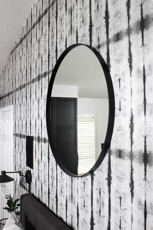 A beautiful Modern Master Bedroom Renovation Reveal! Gorgeous bold wallpaper, black, white and grey tones alongside wooden accent furniture. Ikea cabinets with a sliding barn door. And a white brick fireplace with a dark wooden mantel. Touches of blue and deep red finish the space perfectly. Beautiful transformation! 