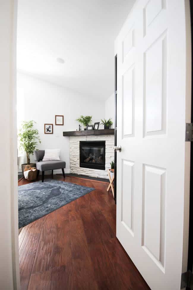 A beautiful Modern Master Bedroom Renovation Reveal! Gorgeous bold wallpaper, black, white and grey tones alongside wooden accent furniture. Ikea cabinets with a sliding barn door. And a white brick fireplace with a dark wooden mantel. Touches of blue and deep red finish the space perfectly. Beautiful transformation! 