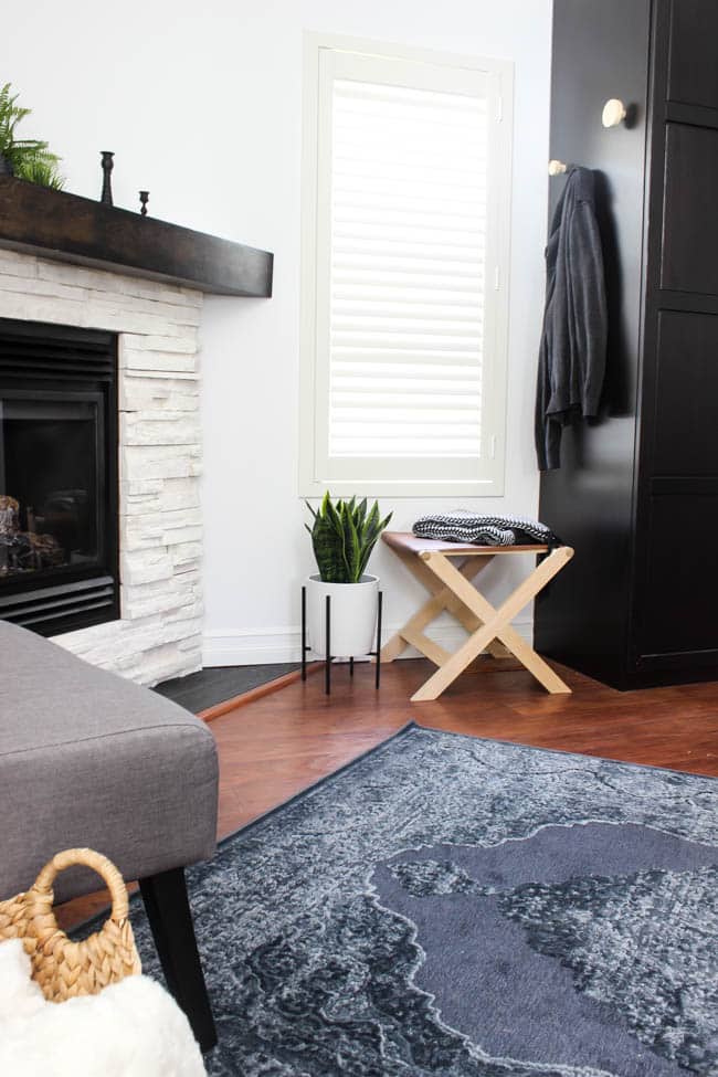 A beautiful Modern Master Bedroom Renovation Reveal! Gorgeous bold wallpaper, black, white and grey tones alongside wooden accent furniture. Ikea cabinets with a sliding barn door. And a white brick fireplace with a dark wooden mantel. Touches of blue and deep red finish the space perfectly. Beautiful transformation! 