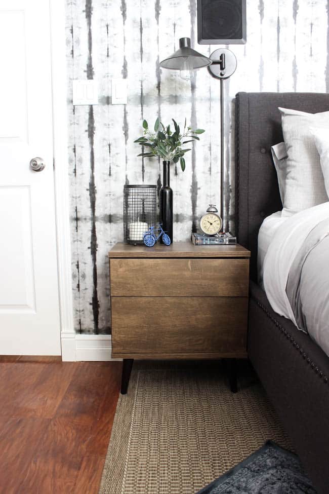 A beautiful Modern Master Bedroom Renovation Reveal! Gorgeous bold wallpaper, black, white and grey tones alongside wooden accent furniture. Ikea cabinets with a sliding barn door. And a white brick fireplace with a dark wooden mantel. Touches of blue and deep red finish the space perfectly. Beautiful transformation! 