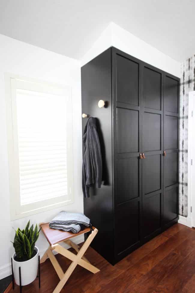 A beautiful Modern Master Bedroom Renovation Reveal! Gorgeous bold wallpaper, black, white and grey tones alongside wooden accent furniture. Ikea cabinets with a sliding barn door. And a white brick fireplace with a dark wooden mantel. Touches of blue and deep red finish the space perfectly. Beautiful transformation! 