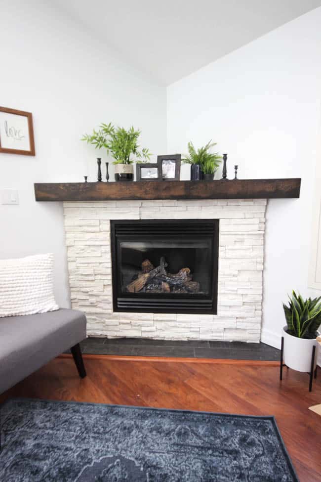 A beautiful Modern Master Bedroom Renovation Reveal! Gorgeous bold wallpaper, black, white and grey tones alongside wooden accent furniture. Ikea cabinets with a sliding barn door. And a white brick fireplace with a dark wooden mantel. Touches of blue and deep red finish the space perfectly. Beautiful transformation! 