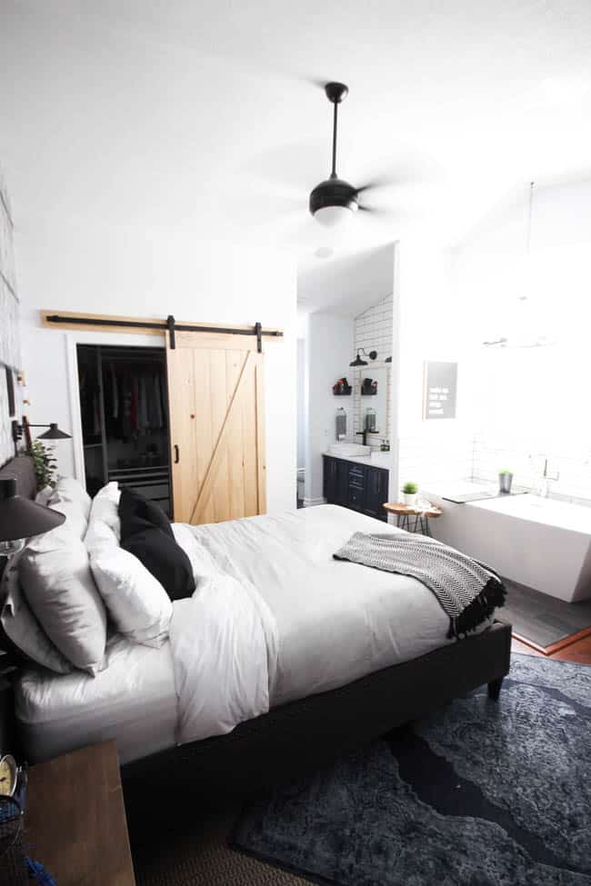 A beautiful Modern Master Bedroom Renovation Reveal! Gorgeous bold wallpaper, black, white and grey tones alongside wooden accent furniture. Ikea cabinets with a sliding barn door. And a white brick fireplace with a dark wooden mantel. Touches of blue and deep red finish the space perfectly. Beautiful transformation!