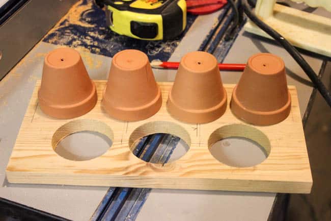 Image of the wooden garden shelf with holes cut and Terra Cotta pots upside down to assist in measuring and spacing of the remaining holes to be cut