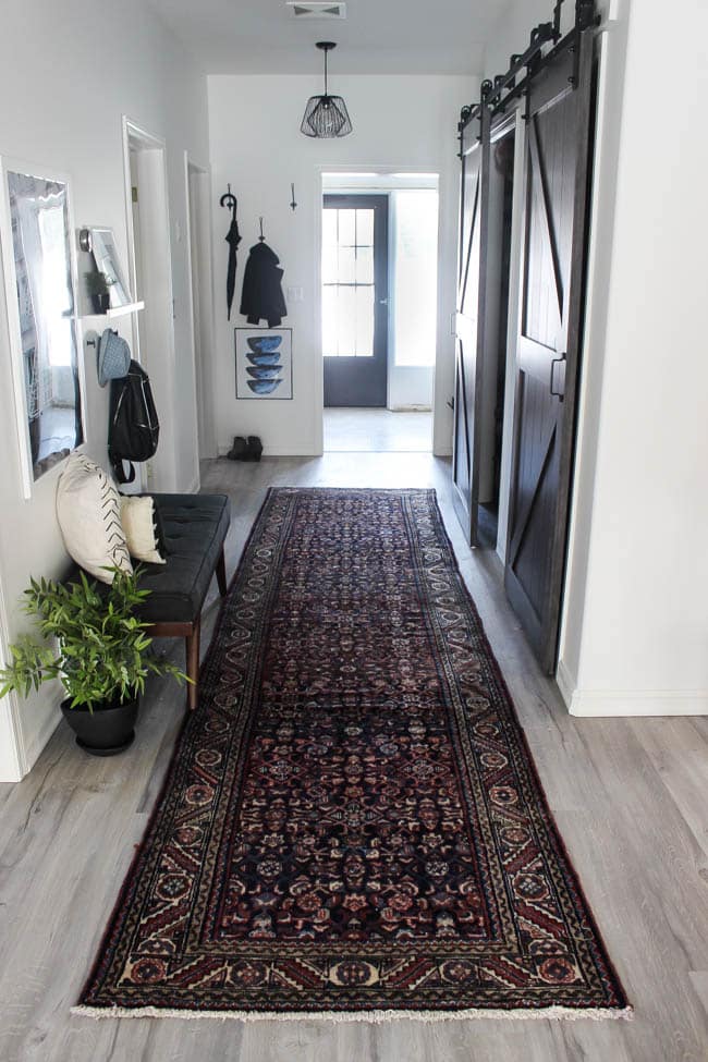 Beautiful hallway decor ideas! Love the eclectic mix of materials and styles in this space. Beautiful light flooring, gorgeous overlapping barn doors, modern artwork, and a vintage hallway runner complete the space. Perfect ideas to fill up a wide hallway!