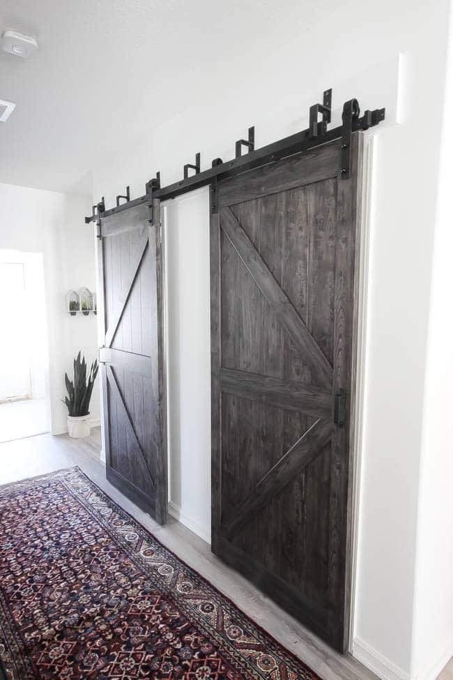 Beautiful hallway decor ideas! Love the eclectic mix of materials and styles in this space. Beautiful light flooring, gorgeous overlapping barn doors, modern artwork, and a vintage hallway runner complete the space. Perfect ideas to fill up a wide hallway!