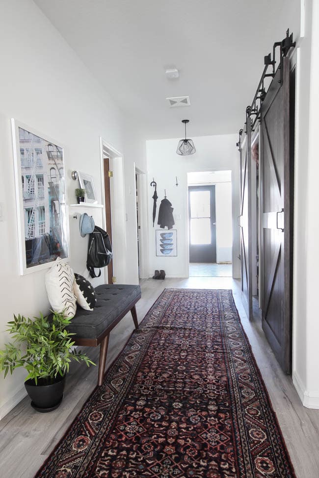 Beautiful hallway decor ideas! Love the eclectic mix of materials and styles in this space. Beautiful light flooring, gorgeous overlapping barn doors, modern artwork, and a vintage hallway runner complete the space. Perfect ideas to fill up a wide hallway!