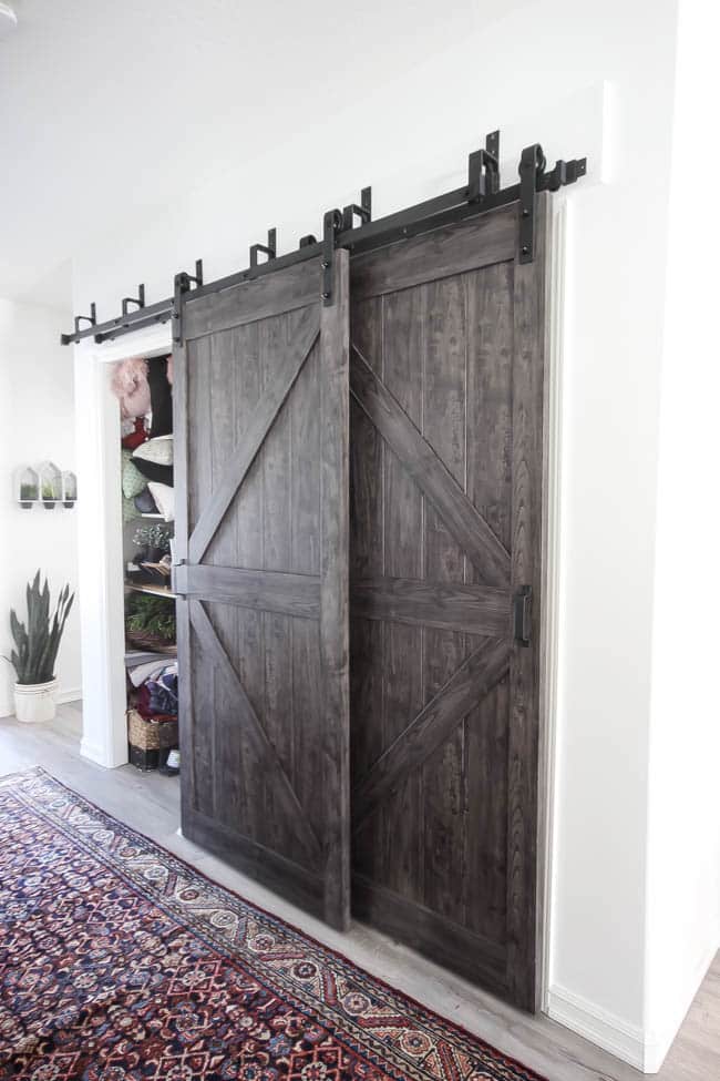 Beautiful hallway decor ideas! Love the eclectic mix of materials and styles in this space. Beautiful light flooring, gorgeous overlapping barn doors, modern artwork, and a vintage hallway runner complete the space. Perfect ideas to fill up a wide hallway!