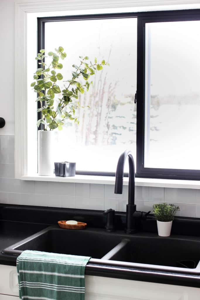 Wow! This stunning modern kitchen was transformed in just one weekend! Love the design ideas in this stunning black and white kitchen! The kitchen features white cabinets, black countertops, black hardware, matte black faucet, black sink, and wood accents. The use of countertop paint and peel and stick tile was brilliant!