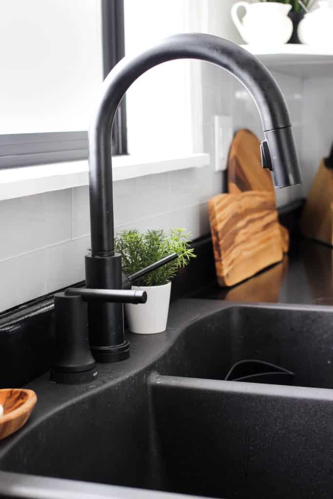 Wow! This stunning modern kitchen was transformed in just one weekend! Love the design ideas in this stunning black and white kitchen! The kitchen features white cabinets, black countertops, black hardware, matte black faucet, black sink, and wood accents. The use of countertop paint and peel and stick tile was brilliant!