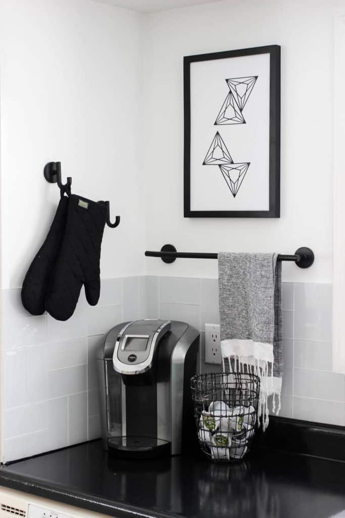 Wow! This stunning modern kitchen was transformed in just one weekend! Love the design ideas in this stunning black and white kitchen! The kitchen features white cabinets, black countertops, black hardware, matte black faucet, black sink, and wood accents. The use of countertop paint and peel and stick tile was brilliant!