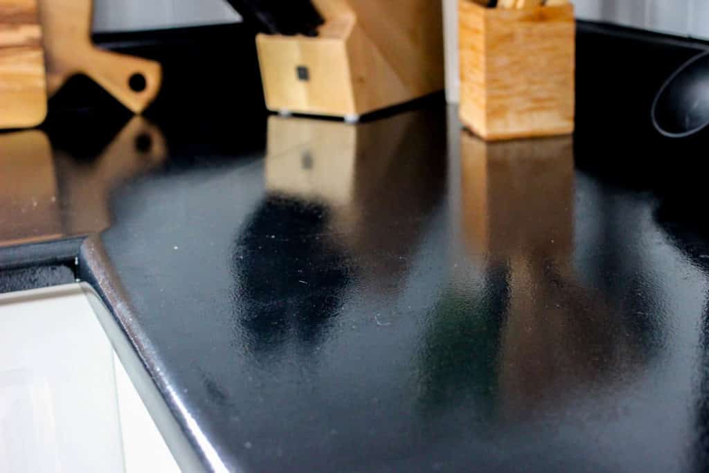 Wow! This stunning modern kitchen was transformed in just one weekend! Love the design ideas in this stunning black and white kitchen! The kitchen features white cabinets, black countertops, black hardware, matte black faucet, black sink, and wood accents. The use of countertop paint and peel and stick tile was brilliant! 