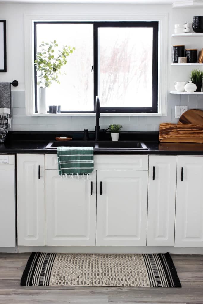 Wow! This stunning modern kitchen was transformed in just one weekend! Love the design ideas in this stunning black and white kitchen! The kitchen features white cabinets, black countertops, black hardware, matte black faucet, black sink, and wood accents. The use of countertop paint and peel and stick tile was brilliant!