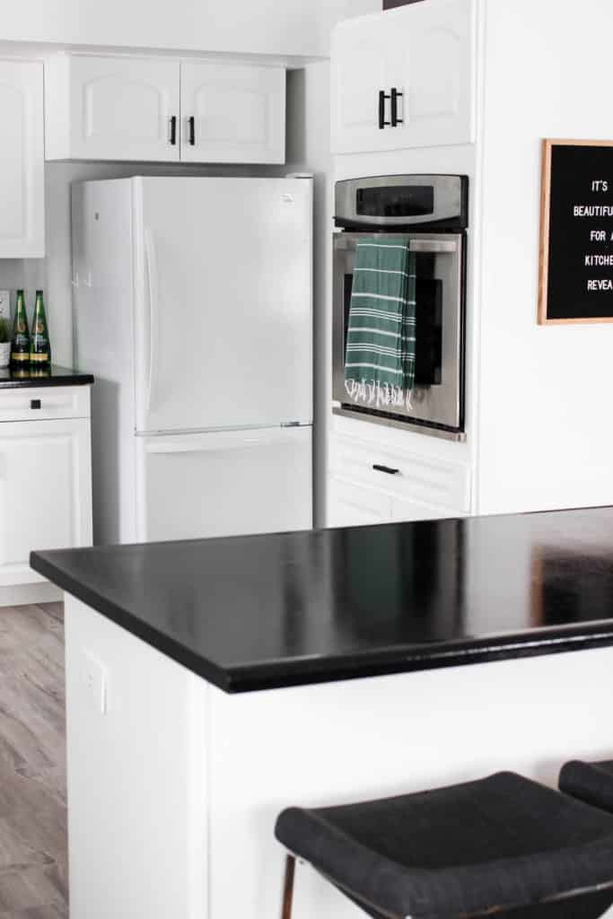 Wow! This stunning modern kitchen was transformed in just one weekend! Love the design ideas in this stunning black and white kitchen! The kitchen features white cabinets, black countertops, black hardware, matte black faucet, black sink, and wood accents. The use of countertop paint and peel and stick tile was brilliant! 