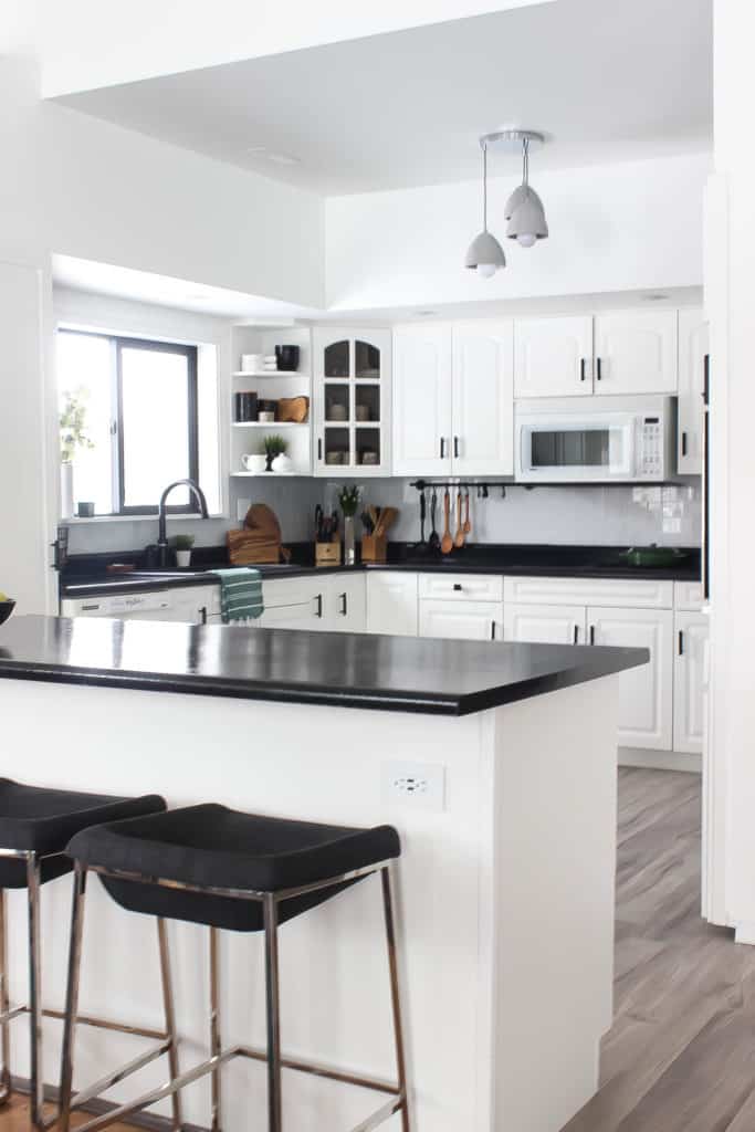 Wow! This stunning modern kitchen was transformed in just one weekend! Love the design ideas in this stunning black and white kitchen! The kitchen features white cabinets, black countertops, black hardware, matte black faucet, black sink, and wood accents. The use of countertop paint and peel and stick tile was brilliant! 