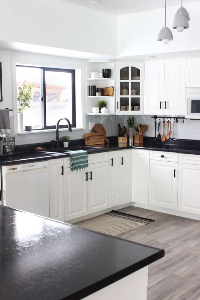 Wow! This stunning modern kitchen was transformed in just one weekend! Love the design ideas in this stunning black and white kitchen! The kitchen features white cabinets, black countertops, black hardware, matte black faucet, black sink, and wood accents. The use of countertop paint and peel and stick tile was brilliant!