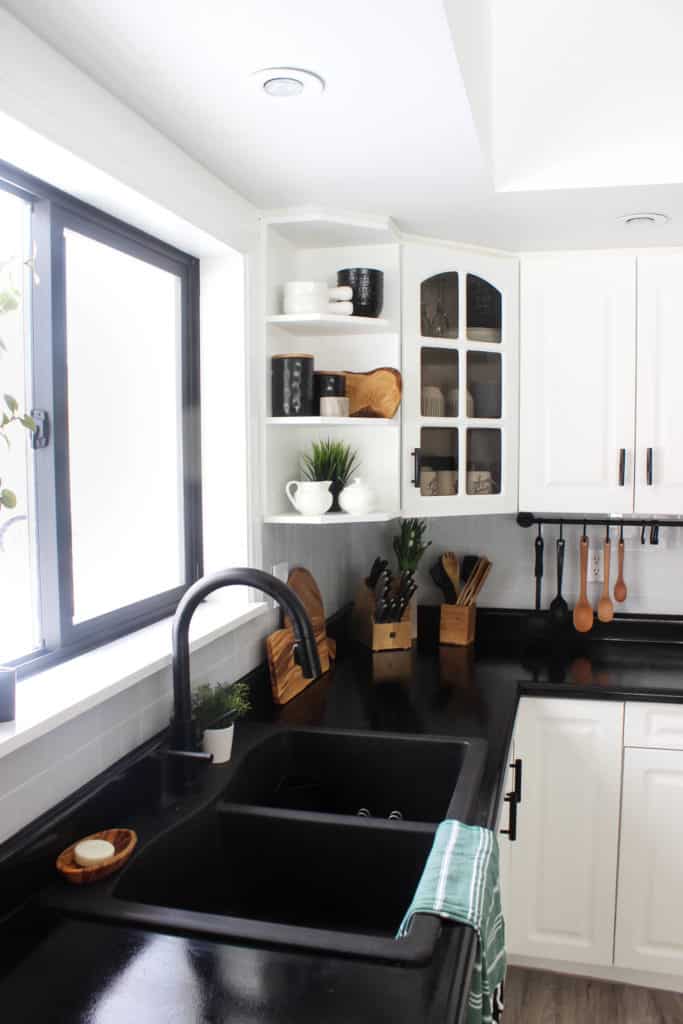 Wow! This stunning modern kitchen was transformed in just one weekend! Love the design ideas in this stunning black and white kitchen! The kitchen features white cabinets, black countertops, black hardware, matte black faucet, black sink, and wood accents. The use of countertop paint and peel and stick tile was brilliant!