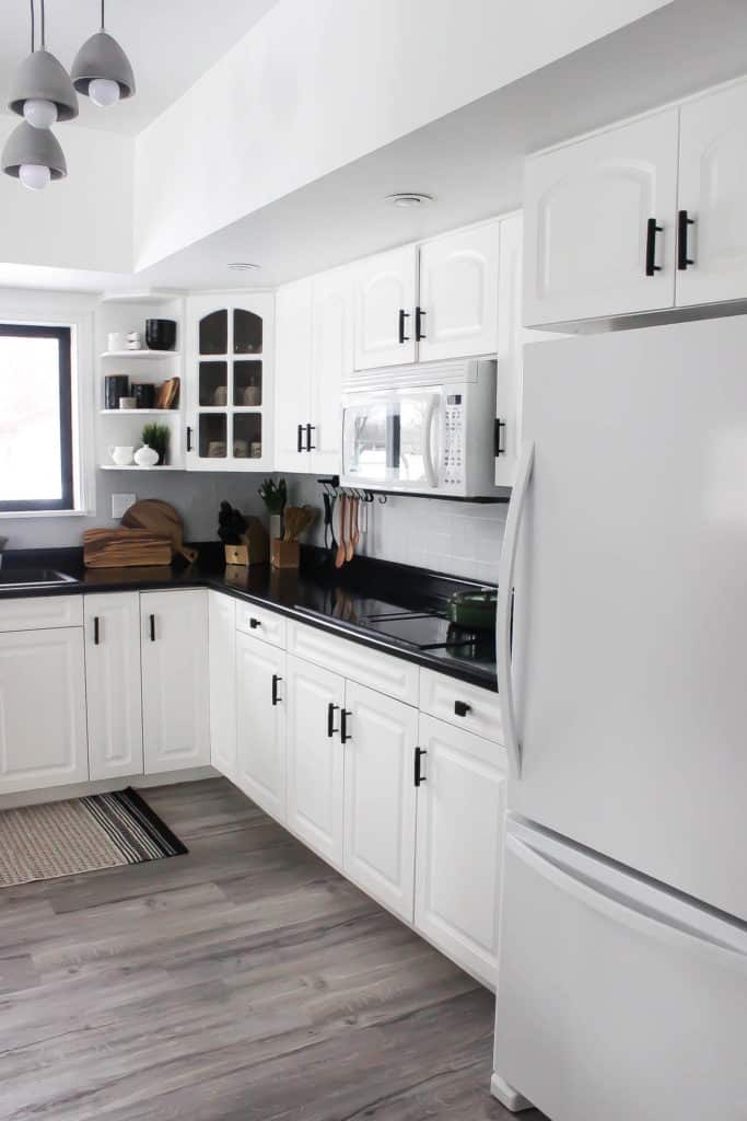 Wow! This stunning modern kitchen was transformed in just one weekend! Love the design ideas in this stunning black and white kitchen! The kitchen features white cabinets, black countertops, black hardware, matte black faucet, black sink, and wood accents. The use of countertop paint and peel and stick tile was brilliant! 