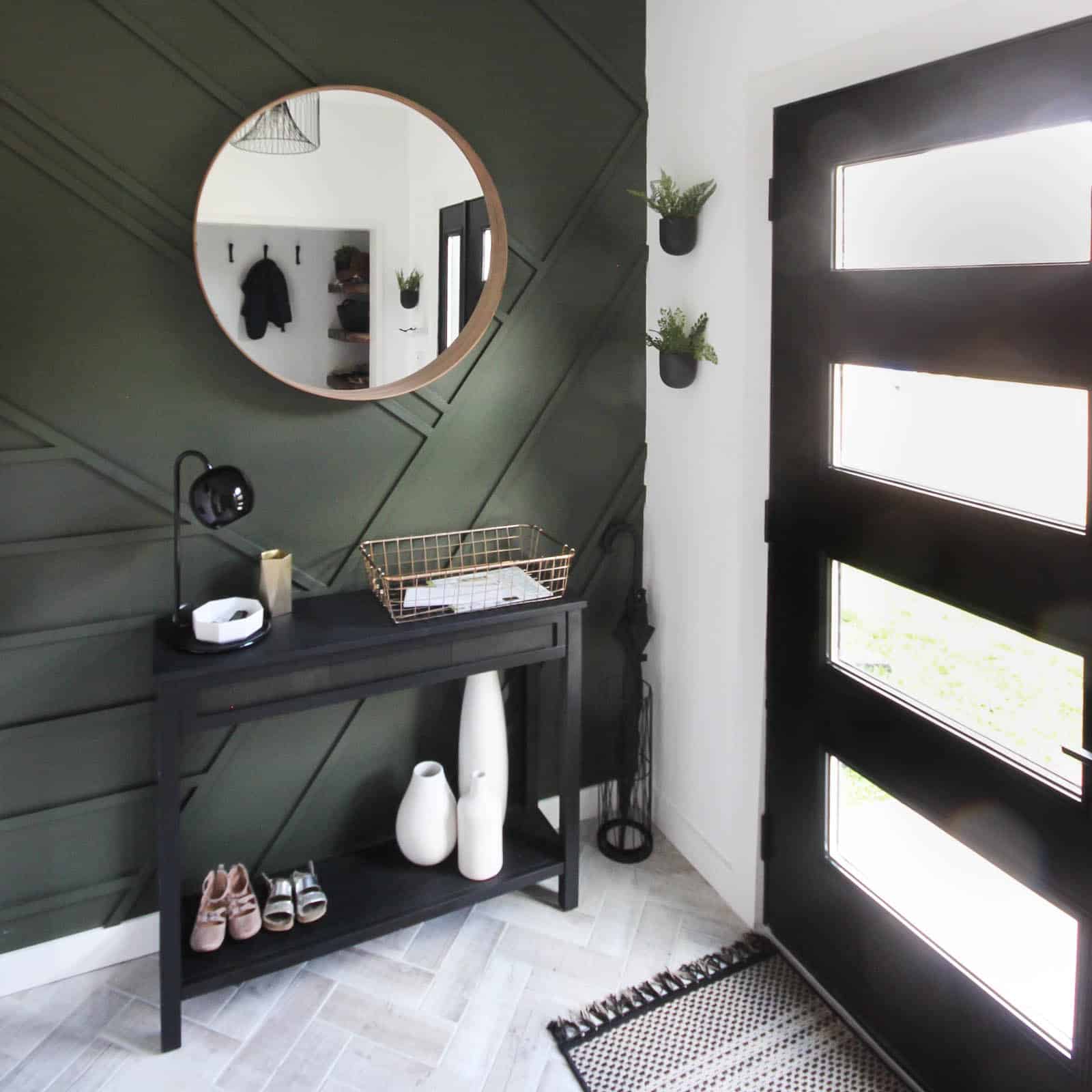 This gorgeous modern entryway reveal is here! What a huge transformation from the outdated space it once was! From the beautiful bench, to the herringbone floors, to the black front door, and the wood accent feature wall. This entry is stunning!