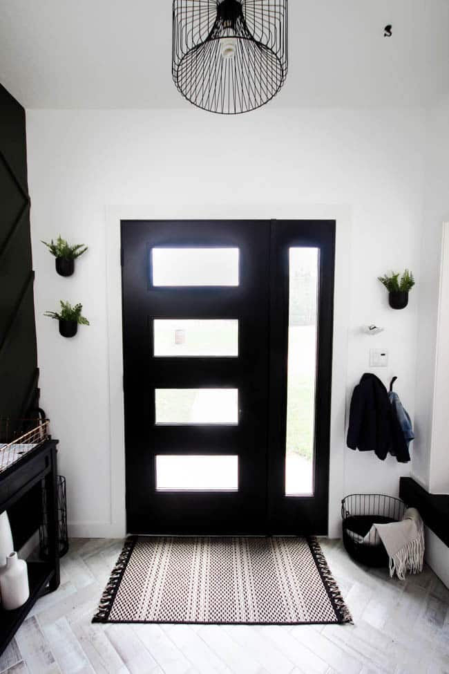 This gorgeous modern entryway reveal is here! What a huge transformation from the outdated space it once was! From the beautiful bench, to the herringbone floors, to the black front door, and the wood accent feature wall. This entry is stunning!