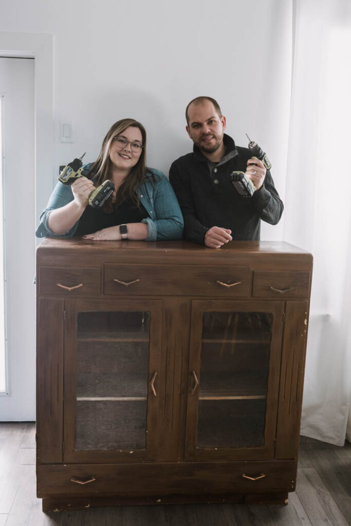 couple standing behind old thrifted cabinet for a makeover