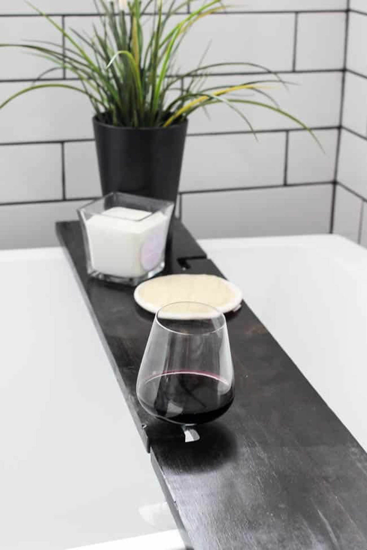 Finished bath tray on bath tub with wine glass, candle, and plant
