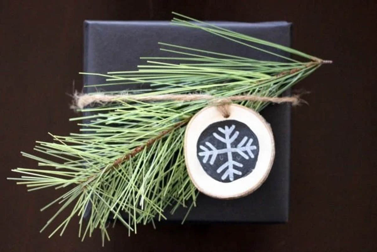 Dark blue rustic gift wrapped present with pine needles and wooden snowflake tag