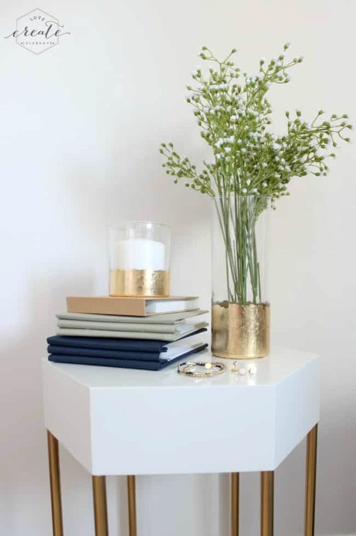 Gold leaf vase on a table with photo albums and a gold leaf candle holder