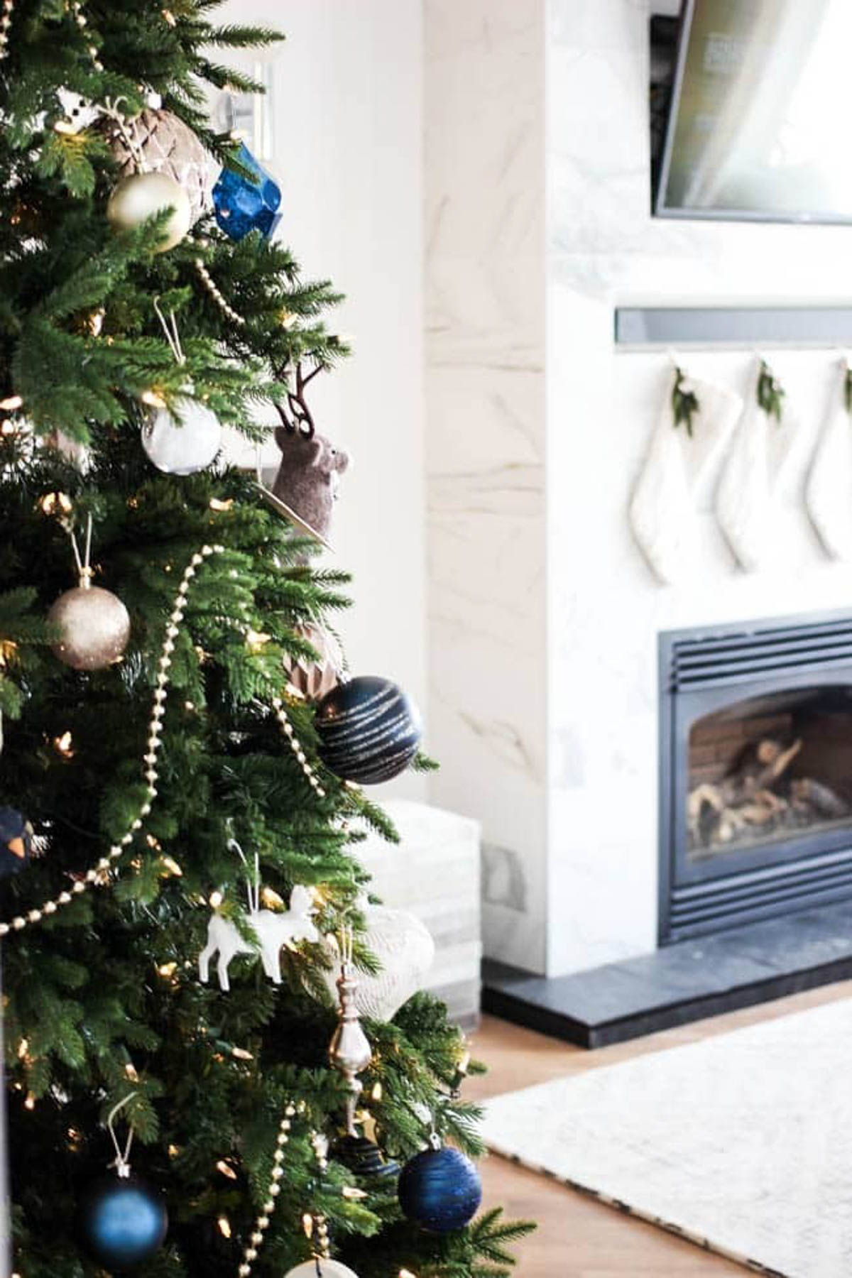 Decorated designer Christmas tree with a fireplace in the background.