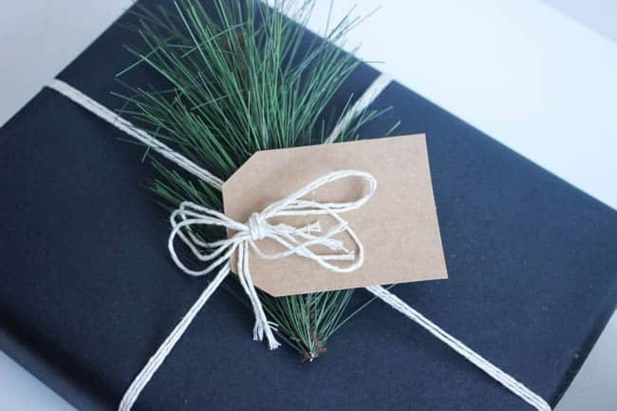 Blue DIY gift wrap with white yarn, tag, and greenery.