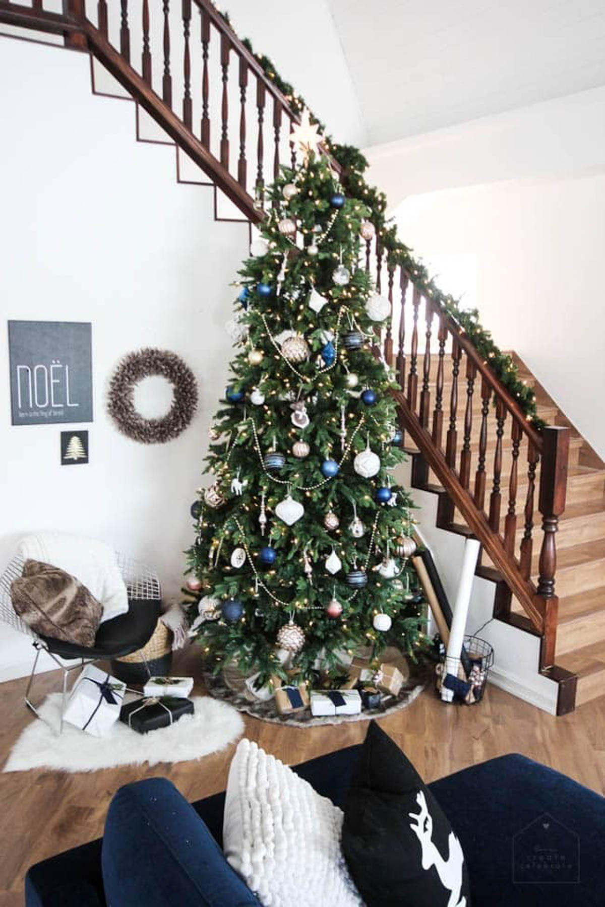 Decorated designer Christmas tree near a couch and stairway.