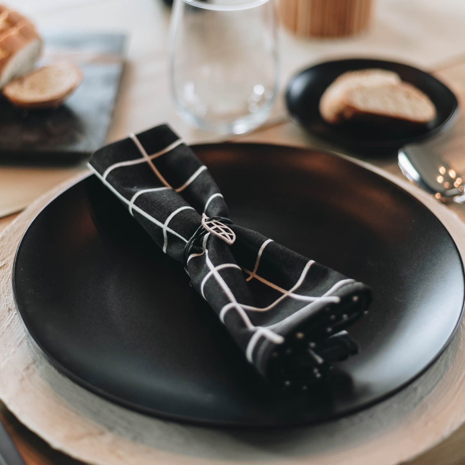 place setting with white charger, black plate, black patterned napkin and minimalist napkin rings