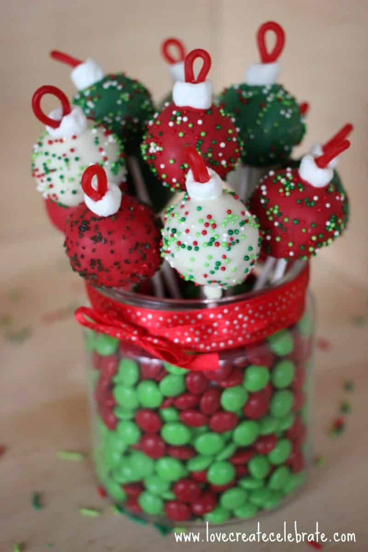 Red, green, and white ornament cake pops in a jar of red and green m&m's.
