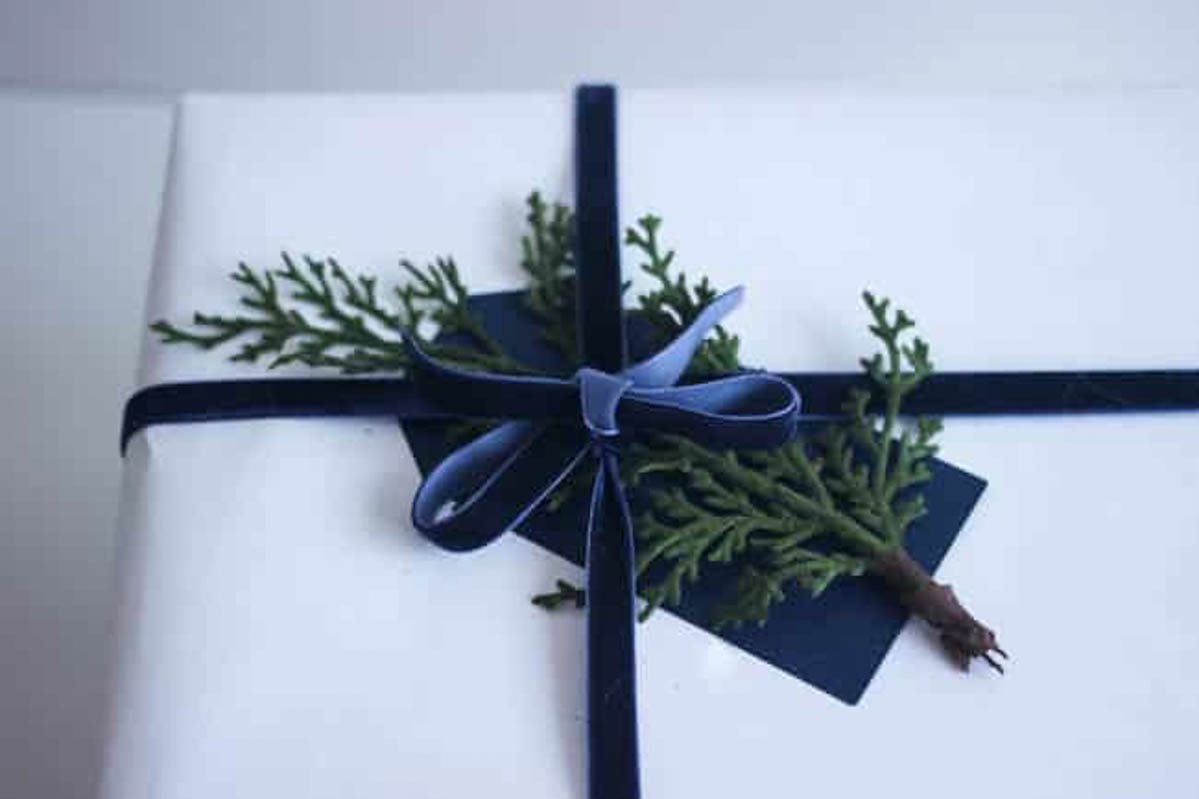 DIY gift wrap with greenery, a blue tag, and a blue velvet ribbon.