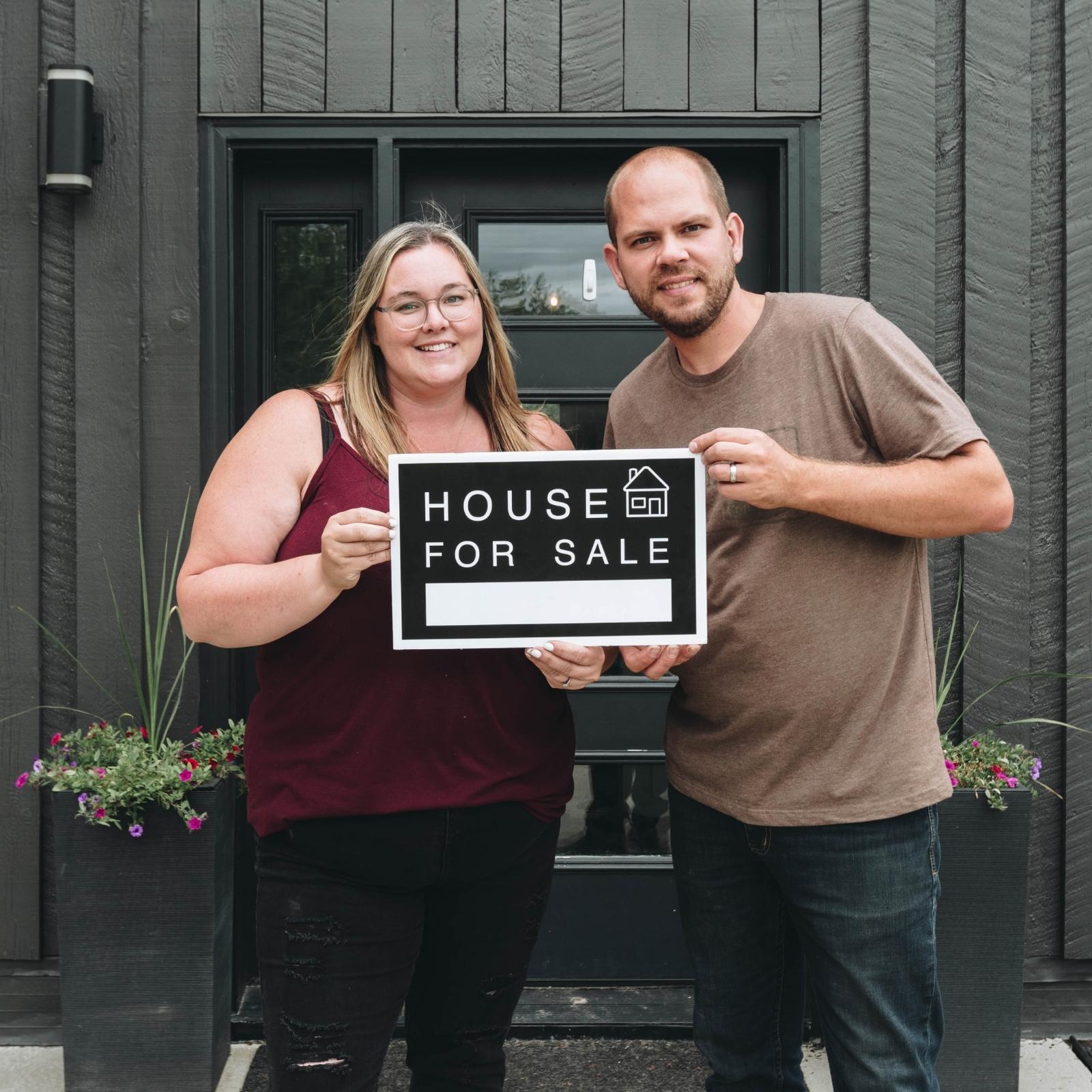 Couple standing with a black house for sale sign